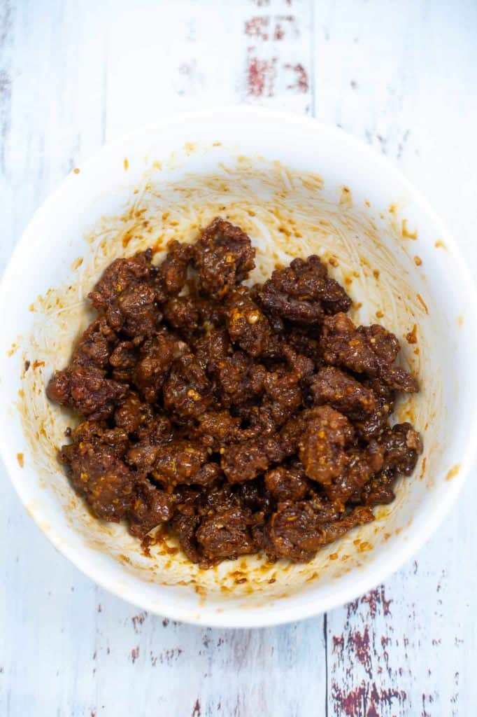 Beef tossed in orange sauce in a white bowl.