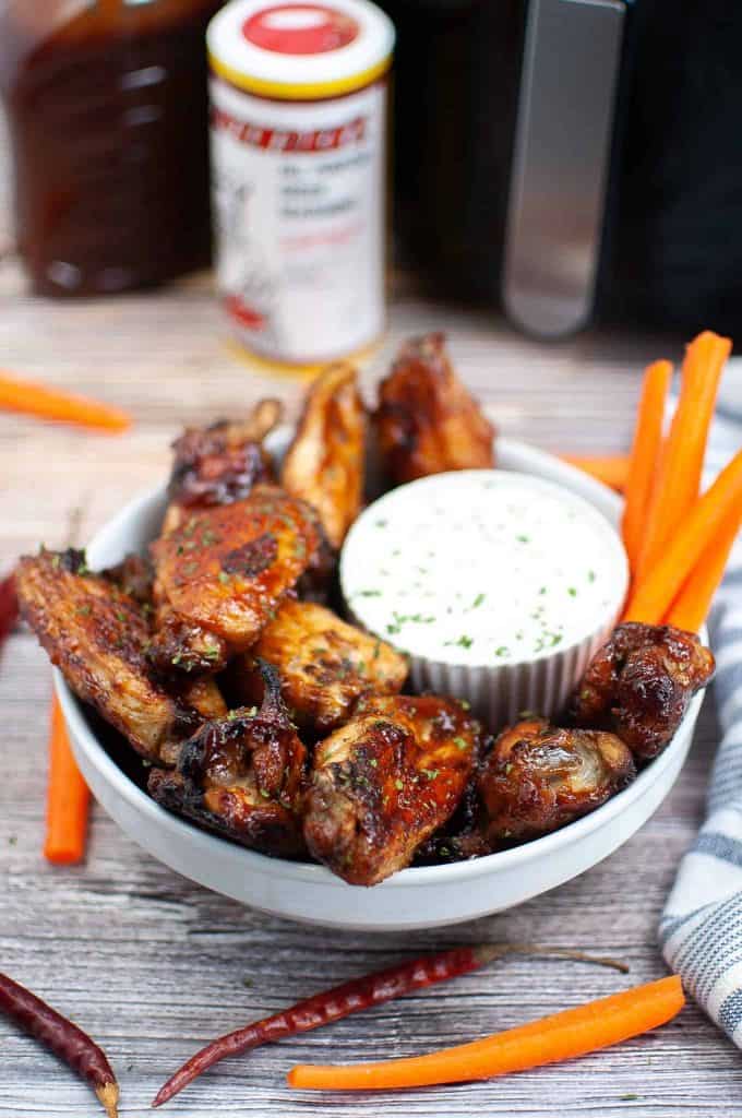 Bowl of BBQ wings with carrots and sauce.