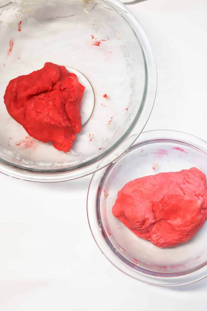 Red cookie dough and pink cookie dough in glass bowls.