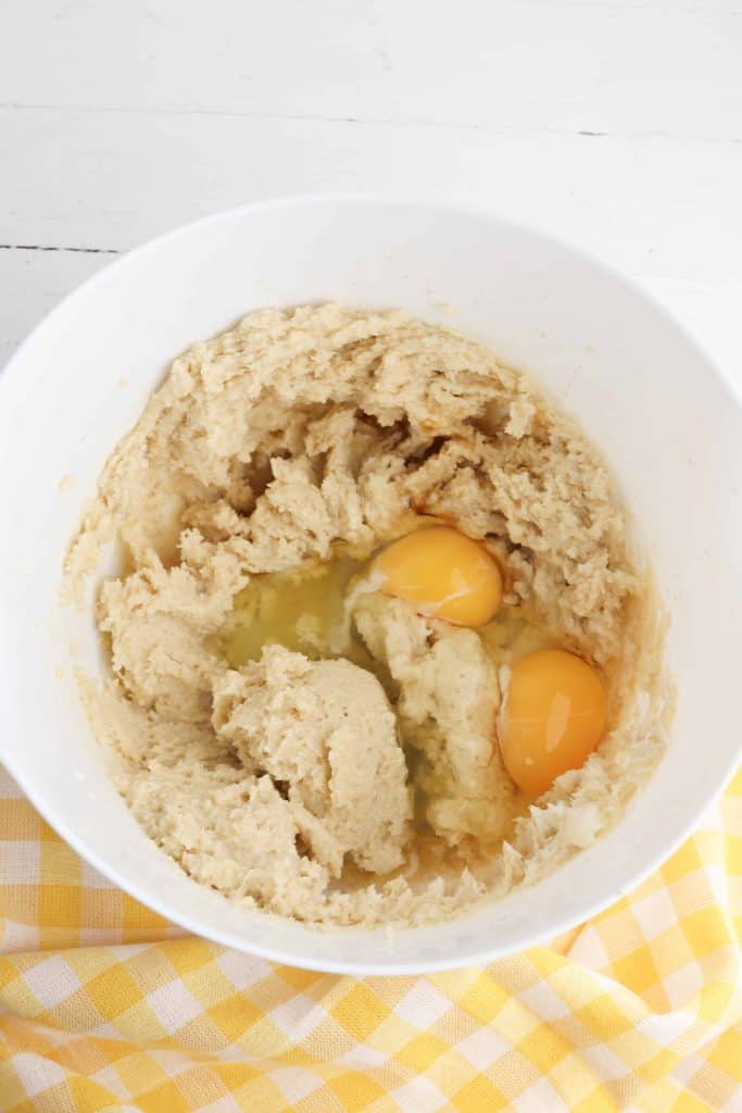 Butter and sugar blended with eggs on top in a white bowl.