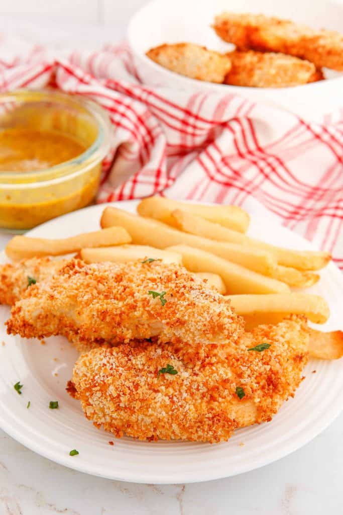 Air fryer chicken tender with French fries on a white plate with honey mustard sauce on the side.