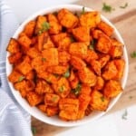 Overhead photo of sweet potato cubes with savory seasoning in a white bowl.