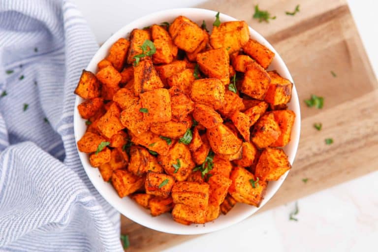 Overhead photo of sweet potato cubes with savory seasoning in a white bowl.
