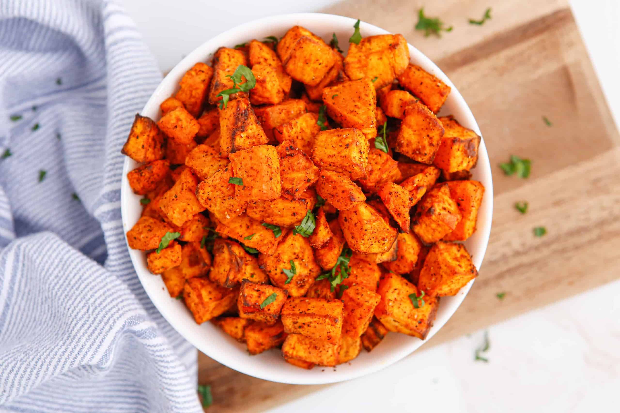 Overhead photo of sweet potato cubes with savory seasoning in a white bowl.