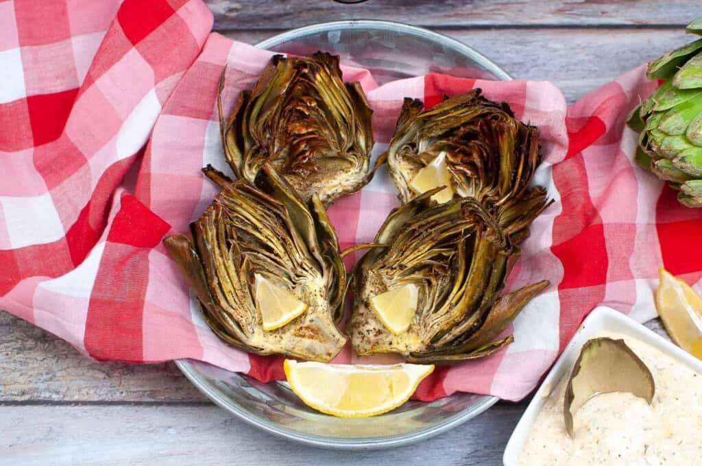 Overhead view of artichokes in a bowl with lemon wedges.