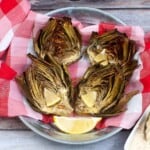 Overhead view of artichokes in a bowl with lemon wedges.