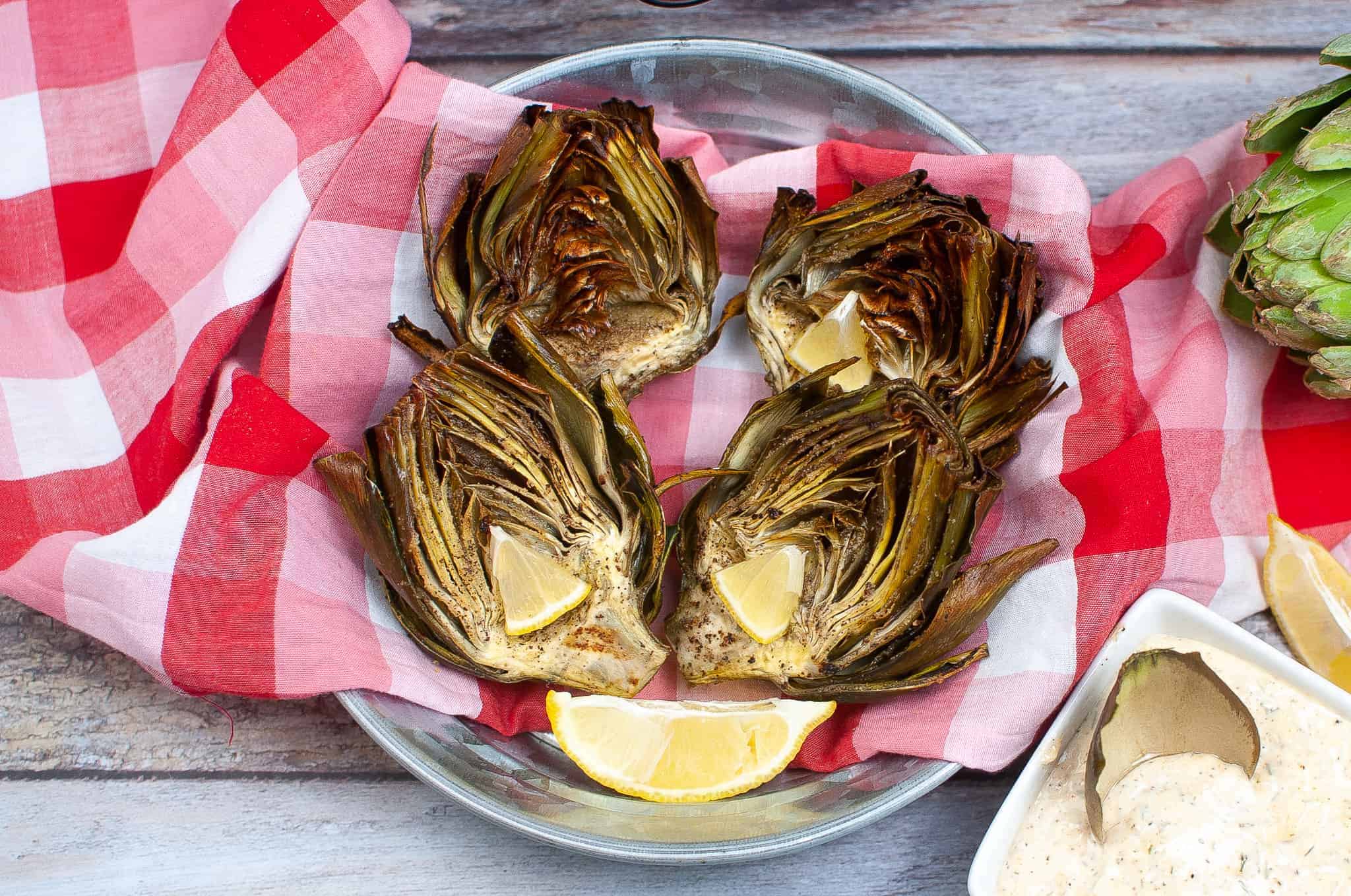Overhead view of artichokes in a bowl with lemon wedges.