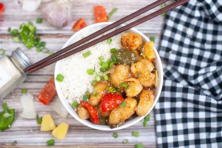 Overhead view of Sweet and Sour Chicken in a white bowl with rice and chopsticks on the side of the bowl.
