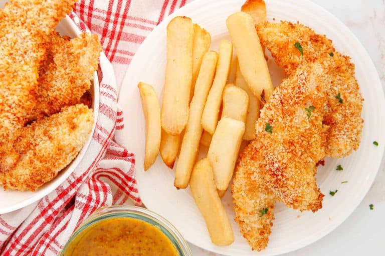 Overhead view of chicken tenders with French fries on a white plate.
