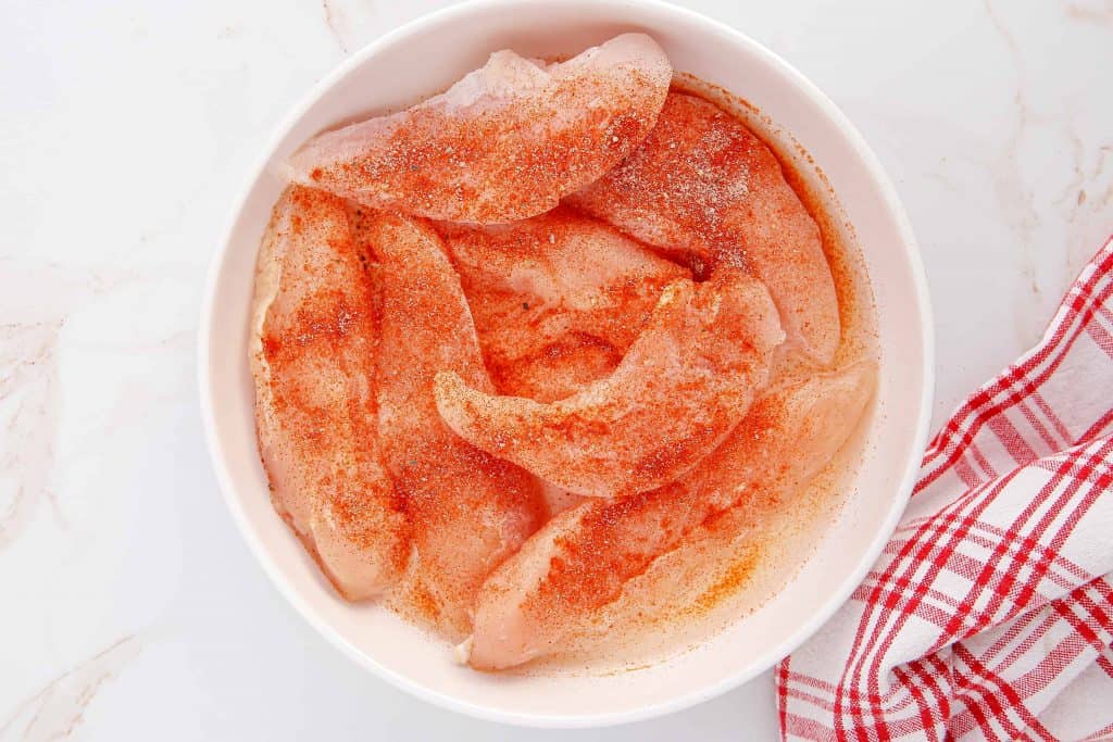 Seasoned chicken tenders in a white bowl.