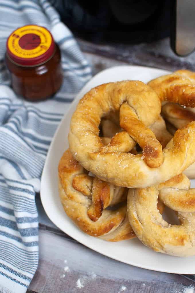 Soft pretzels on a white plate with a bottle of yeast behind it.