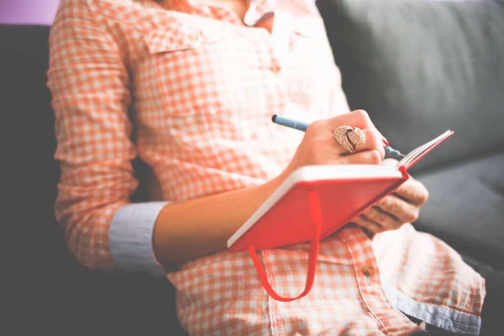 Lady in an orange gingham dress writing in a journal.