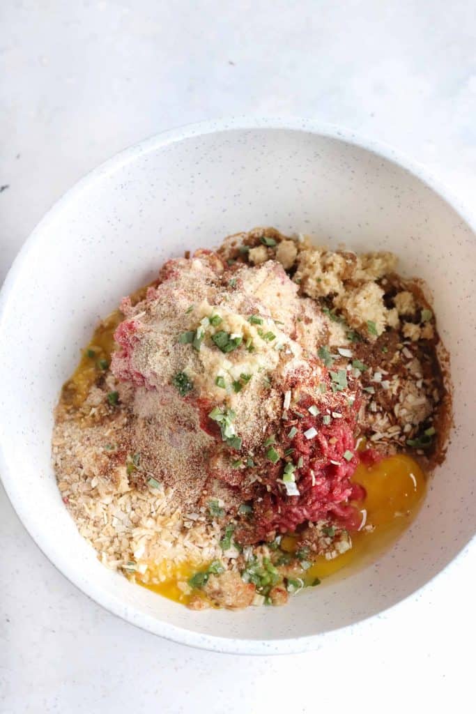 Ground beef, bread crumbs and seasoning in a white bowl.
