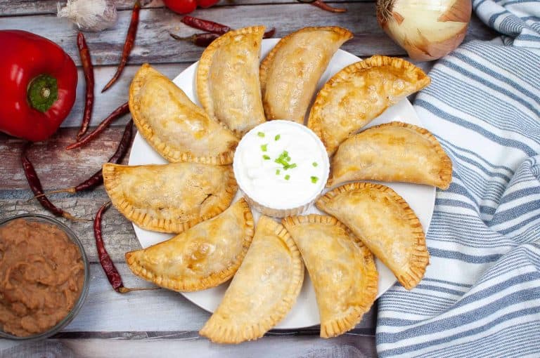 Overhead view of beef empanadas with sour cream sauce.