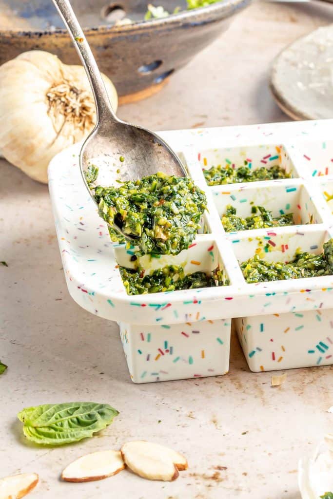 Scooping pesto into ice cube tray.