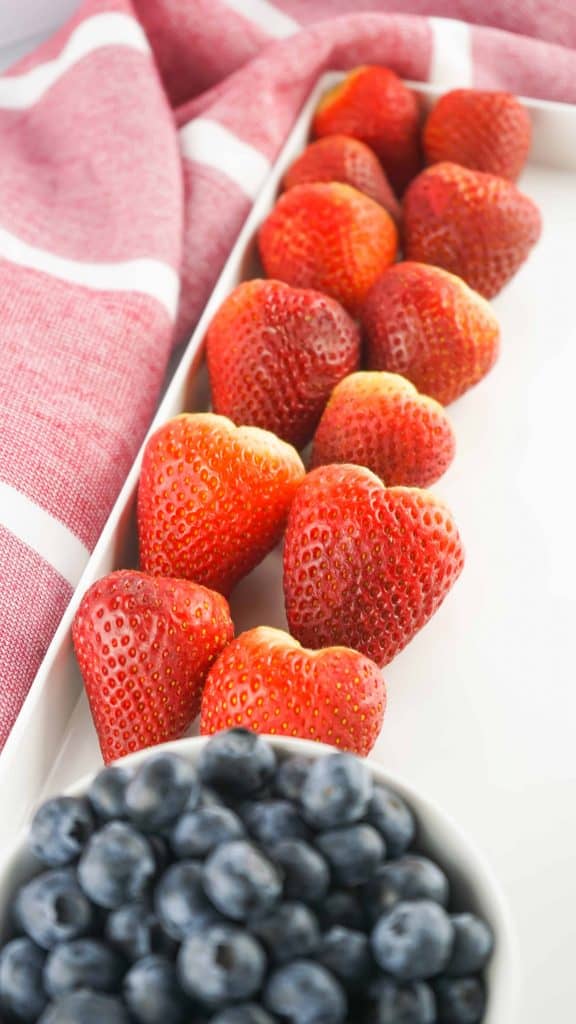 Row of strawberries and a bowl of blueberries.