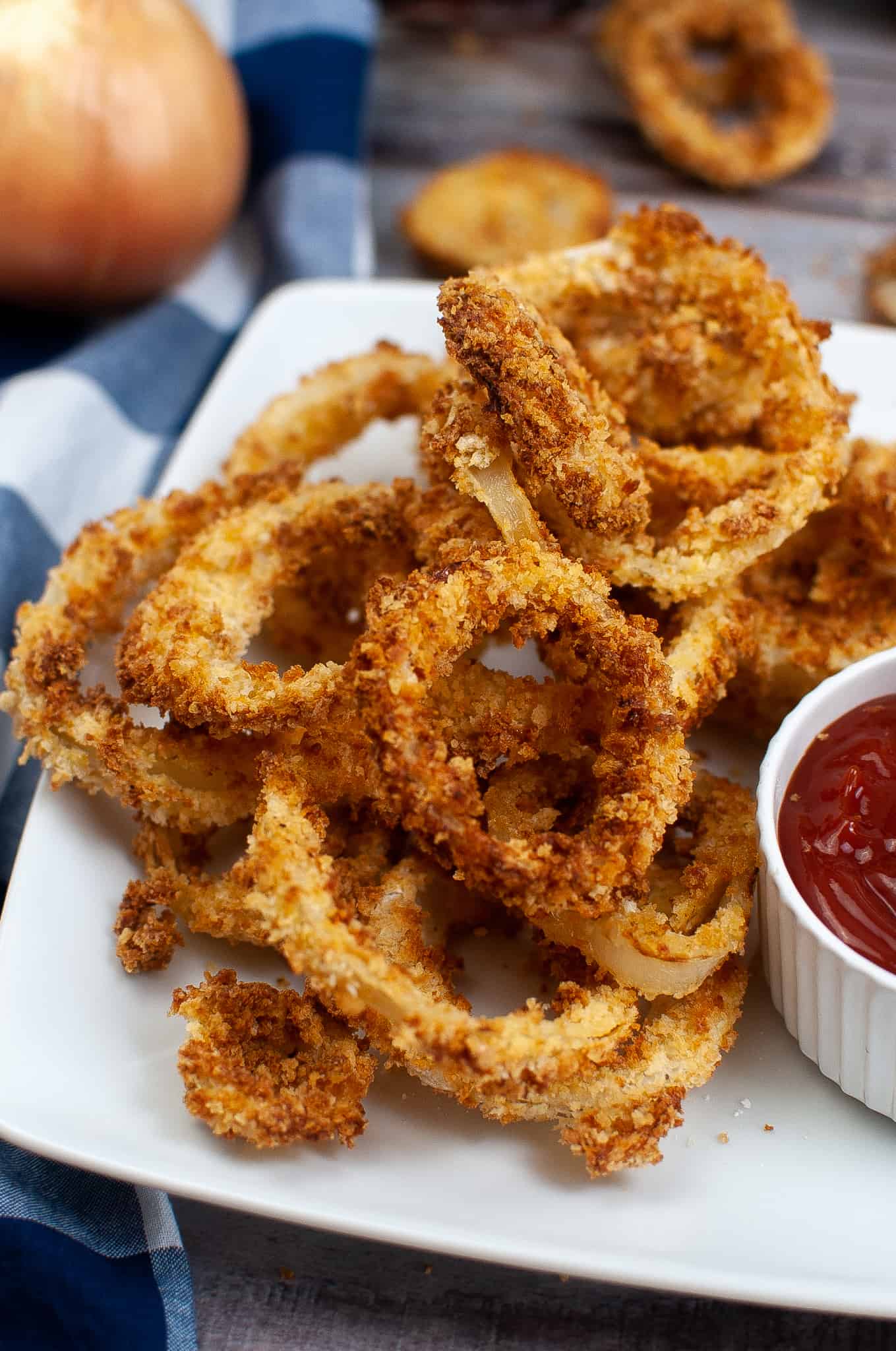 closeup of onion rings on a white square plate with ketchup on the side.