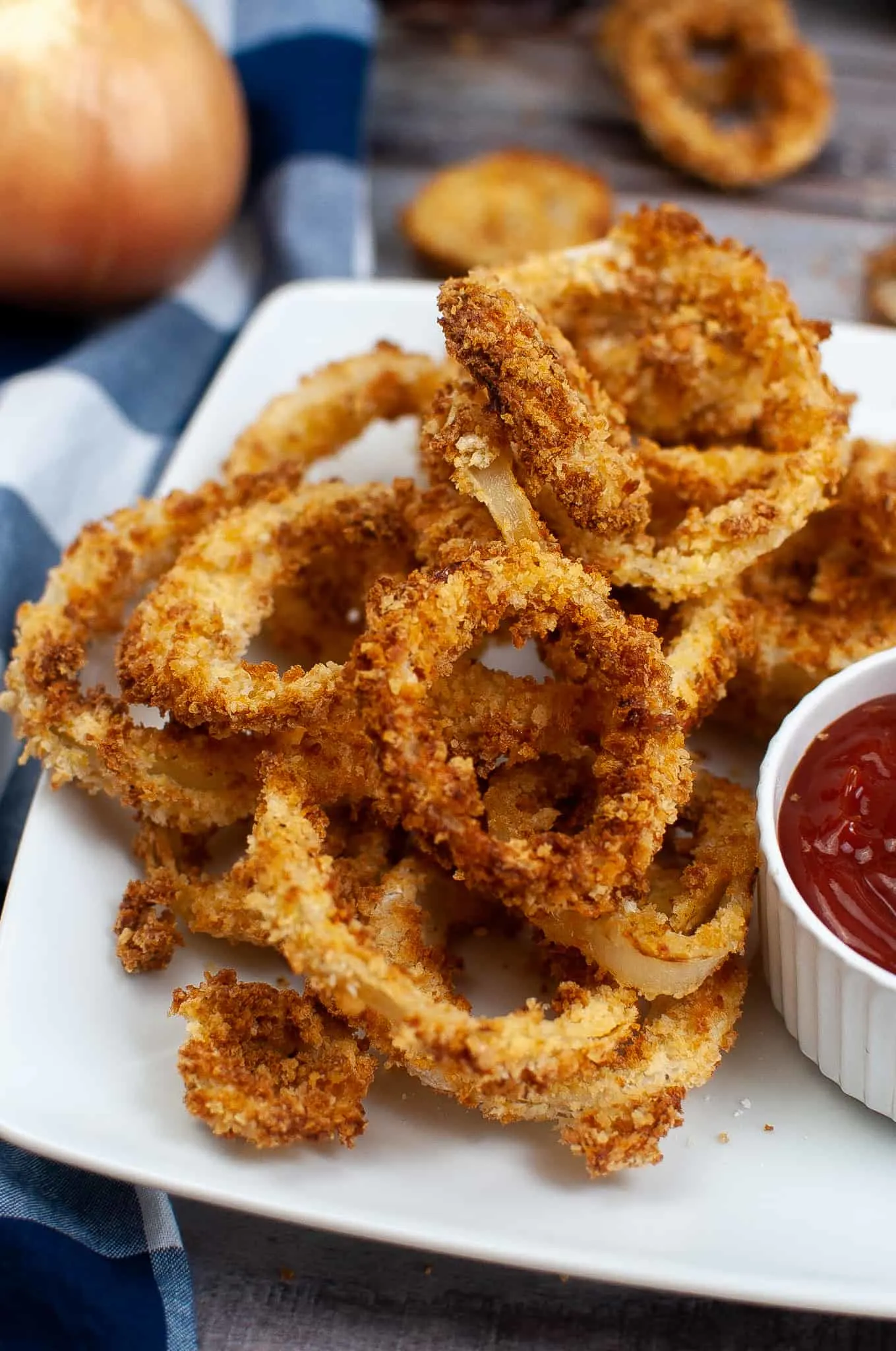 closeup of onion rings on a white square plate with ketchup on the side.