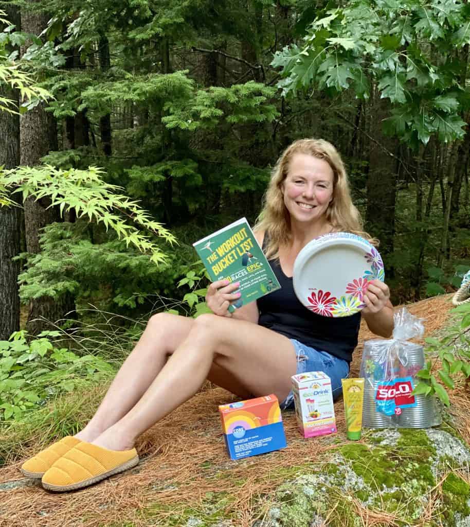 Lady sitting outside on a rock holding a book and paper plates with other products in front of her.