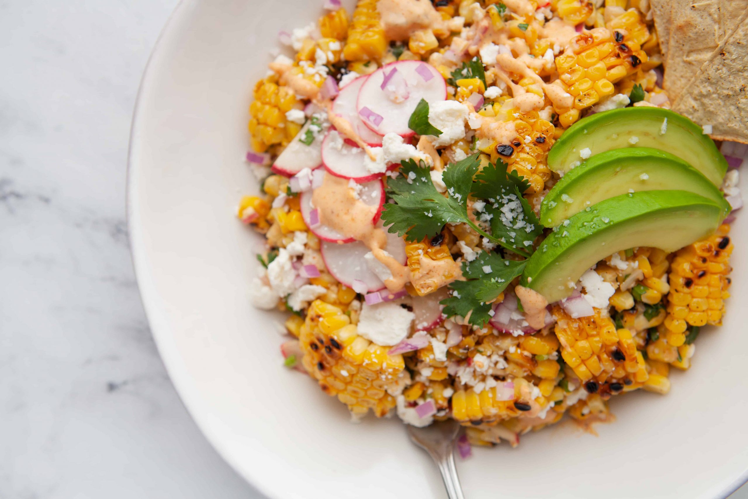 Corn in bowl with avocado and radish slices.