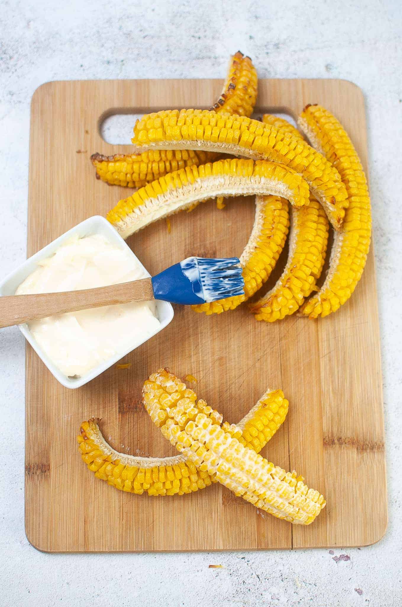 Brushing mayonnaise on corn ribs.
