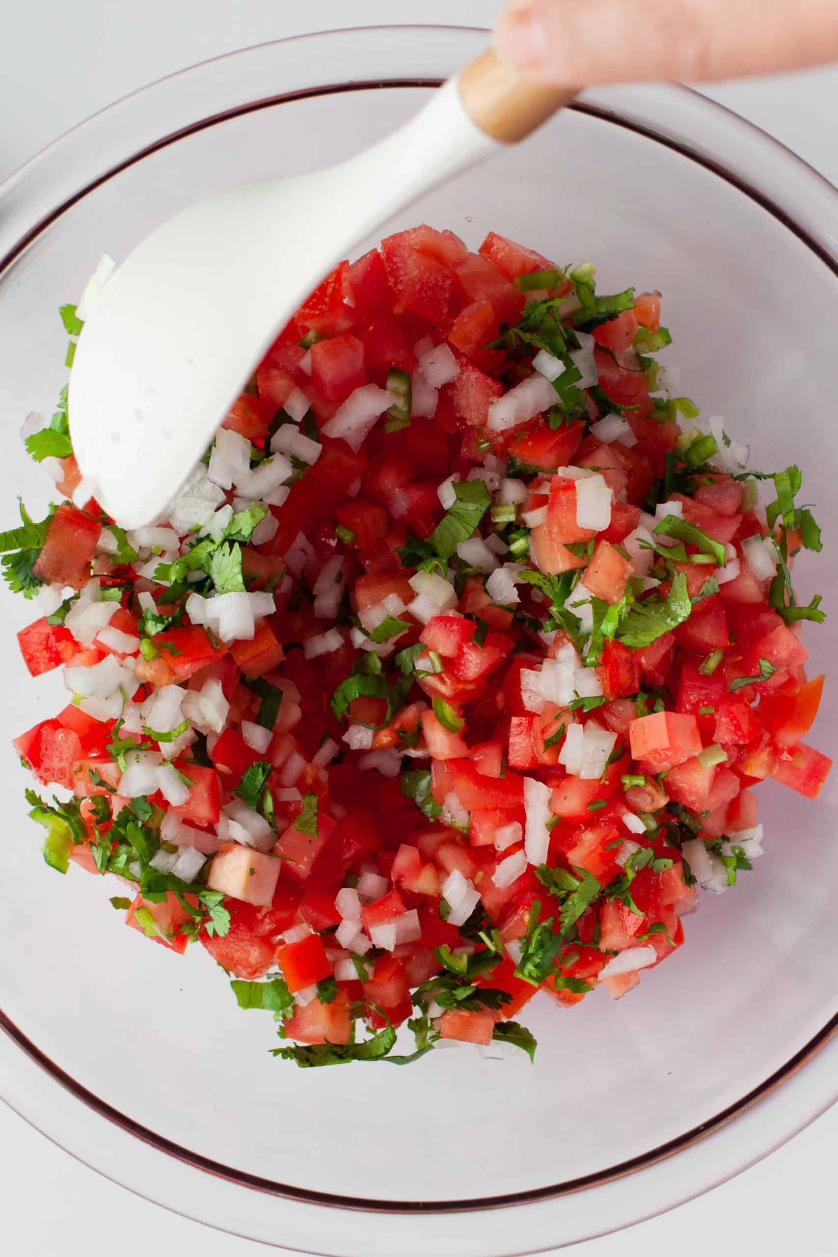 Stirring salsa fresca in a glass bowl.