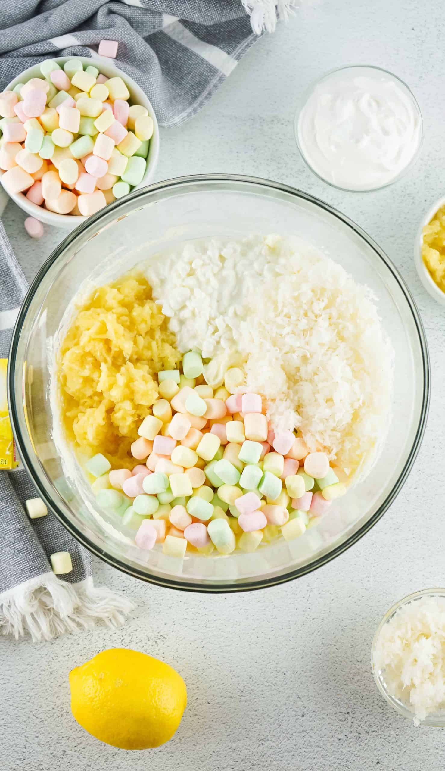 Overhead view of fruity mini marshmallows, crushed pineapple, shredded coconut and cottage cheese in a glass bowl.