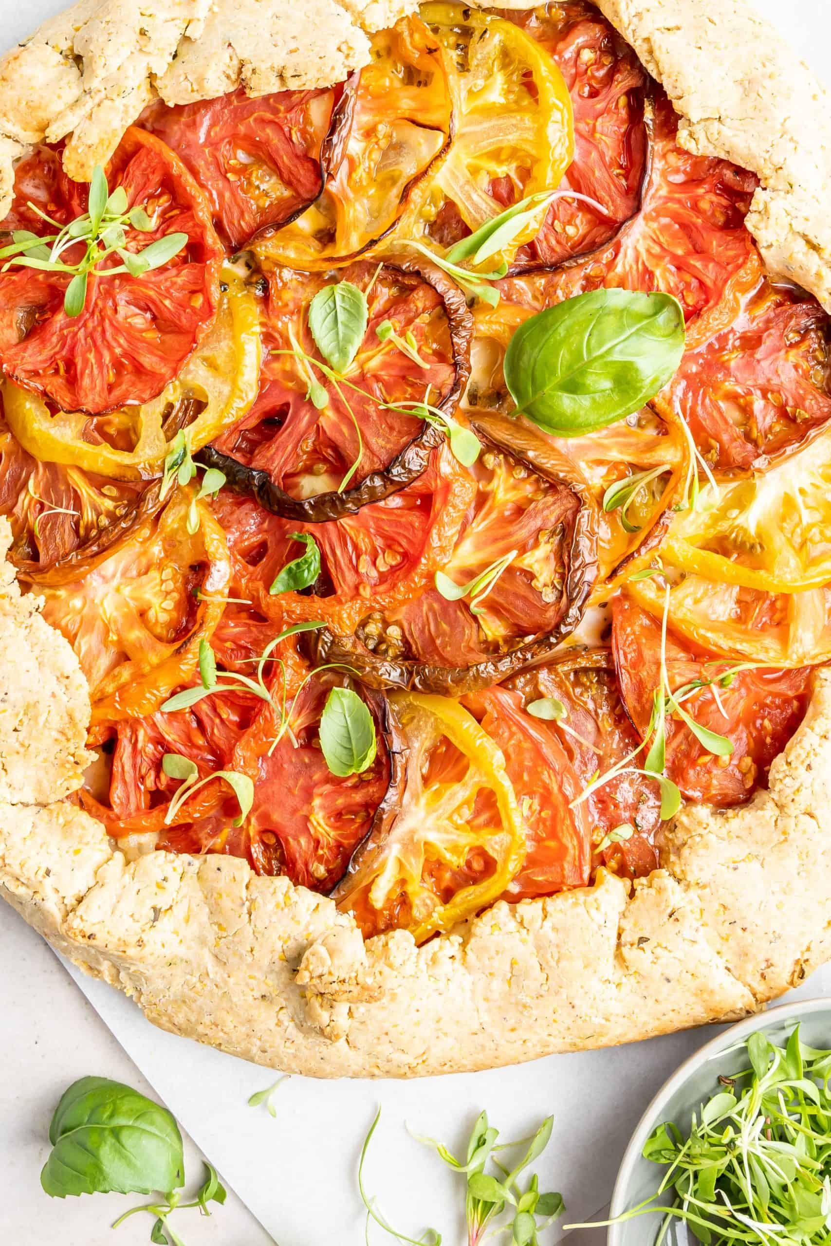 Overhead view of baked galette with tomatoes and fresh herbs.