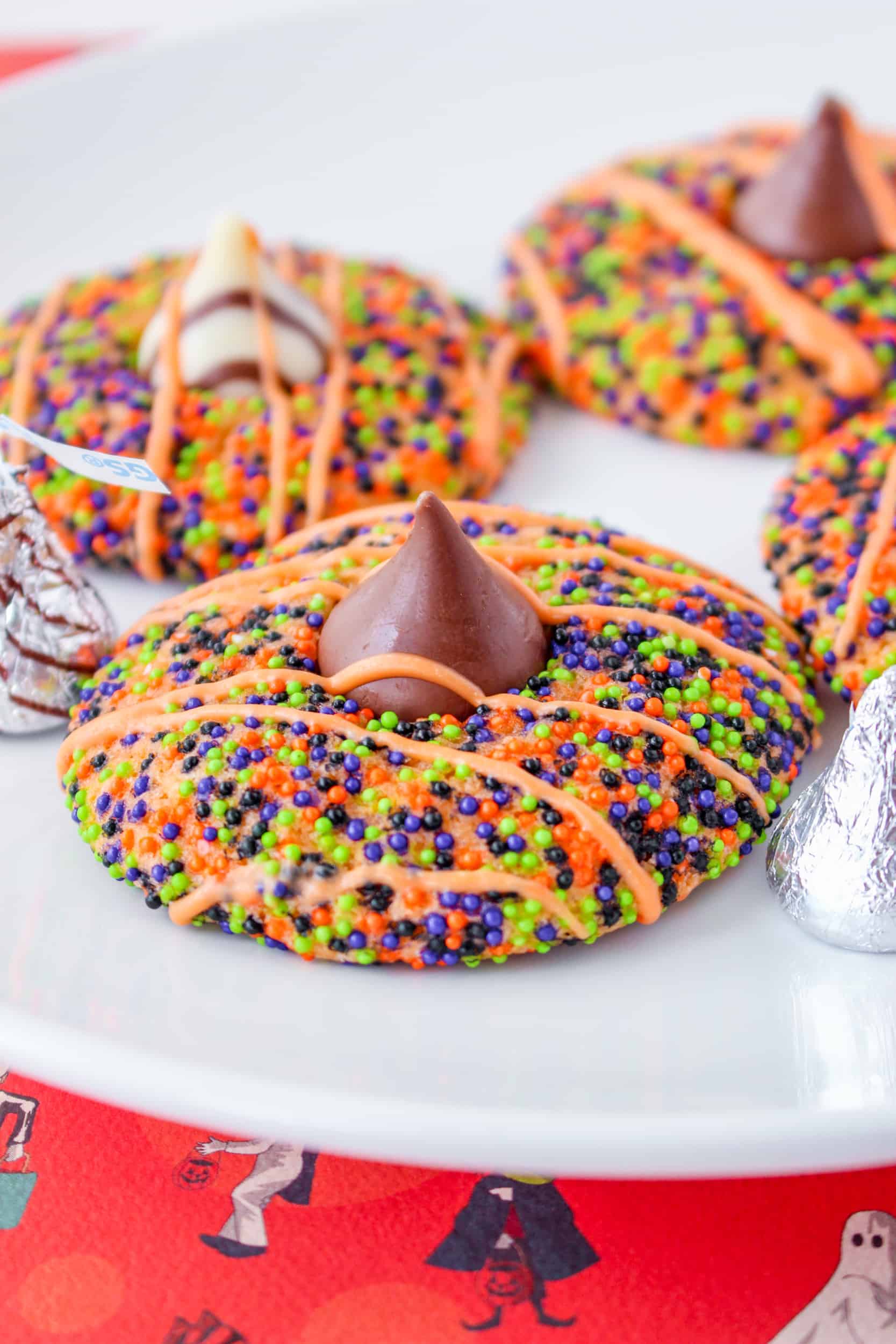 Halloween cookies with sprinkles, Hershey kisses and orange icing drizzled on top.