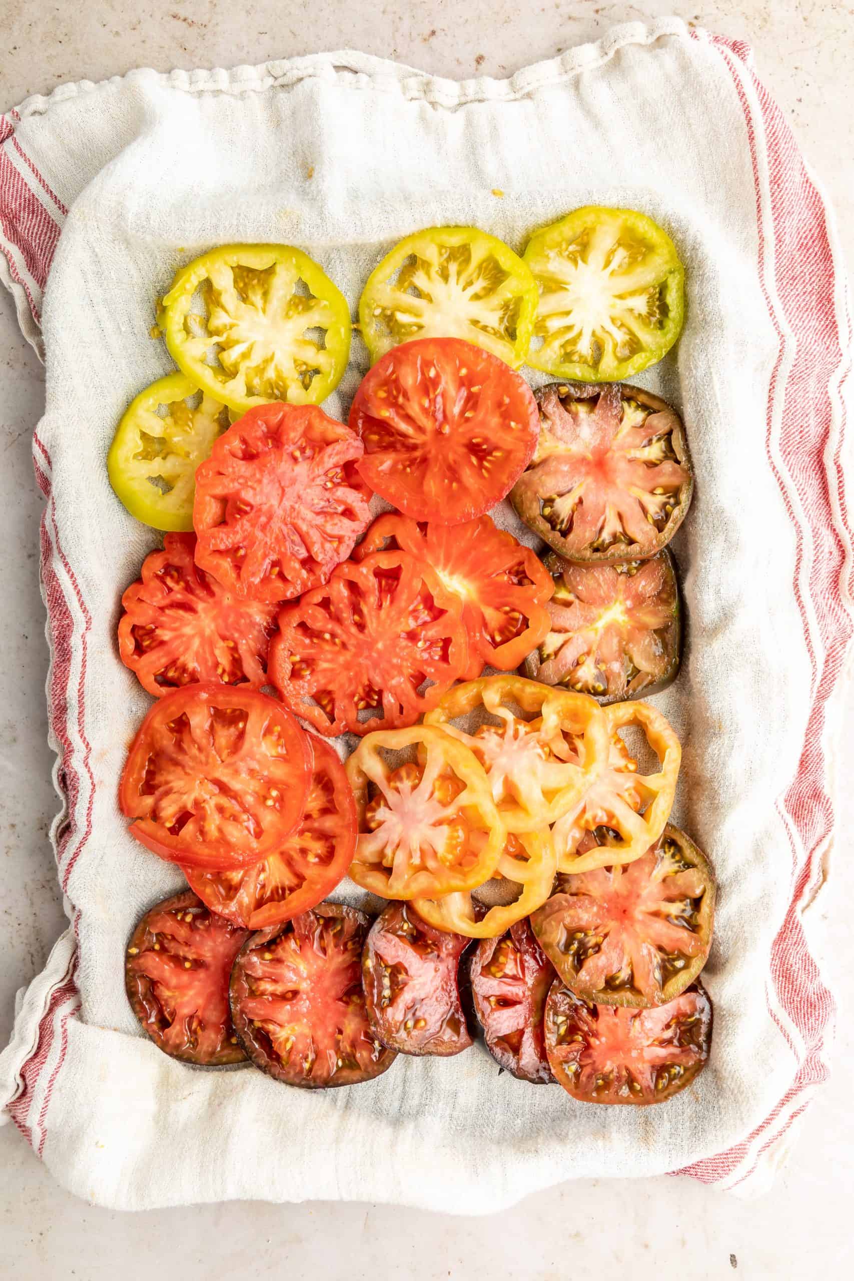 Overhead view of sliced heirloom tomatoes on a clean dish towel.