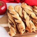 Apple butter twists with cinnamon sugar on a cutting board with an apple behind it.