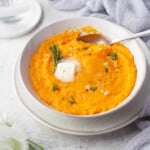 Mashed butternut squash in a bowl with herbs and butter.