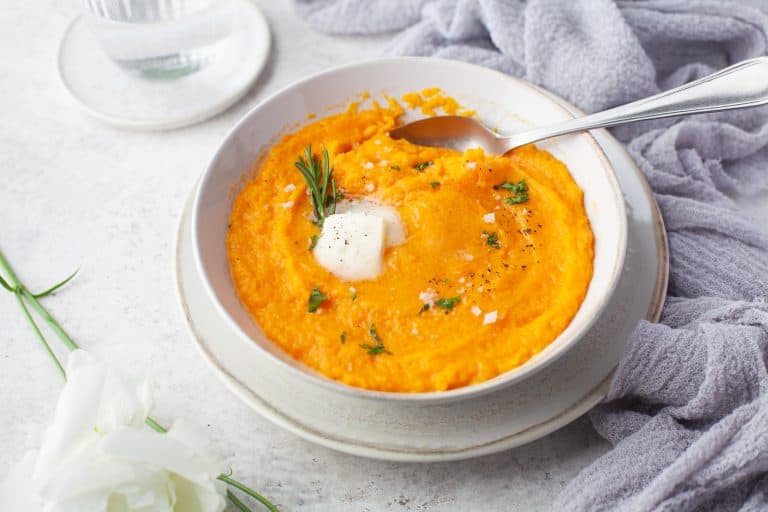 Mashed butternut squash in a bowl with herbs and butter.