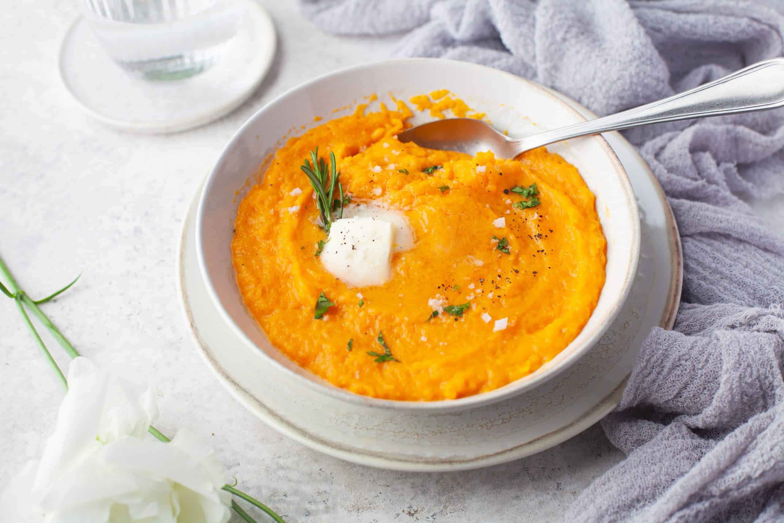 Mashed butternut squash in a bowl with herbs and butter.