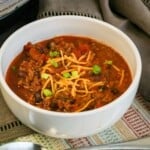 Chili with cheese and beans and green onions in a white bowl.