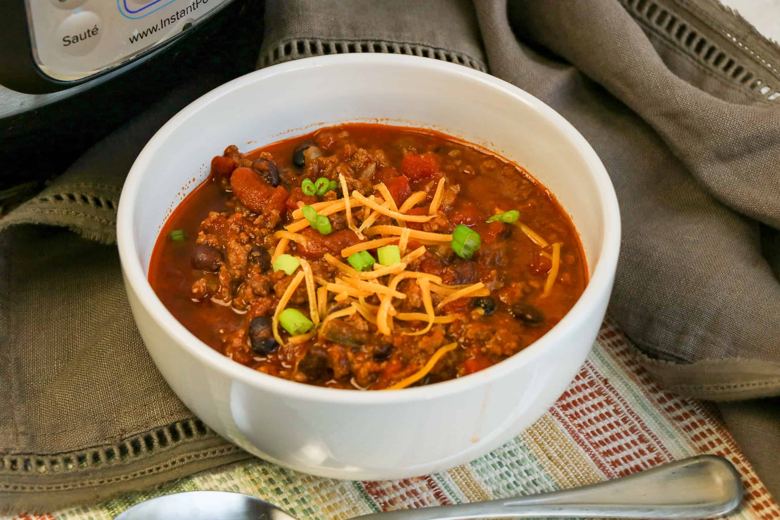 Chili with cheese and beans and green onions in a white bowl.