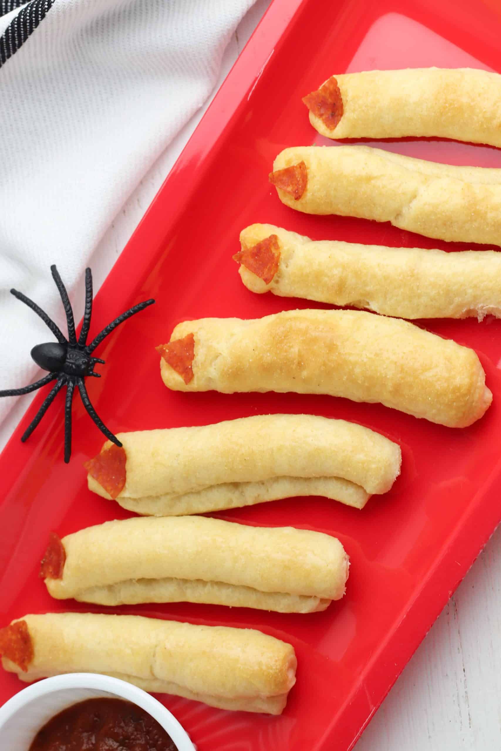 Red plate with witch's fingers breadsticks on it and plastic spider.