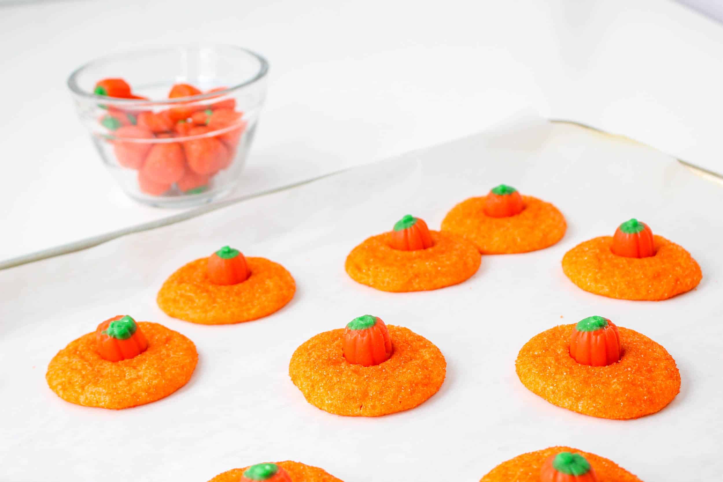 Orange cookies with candy pumpkins on a sheet pan.