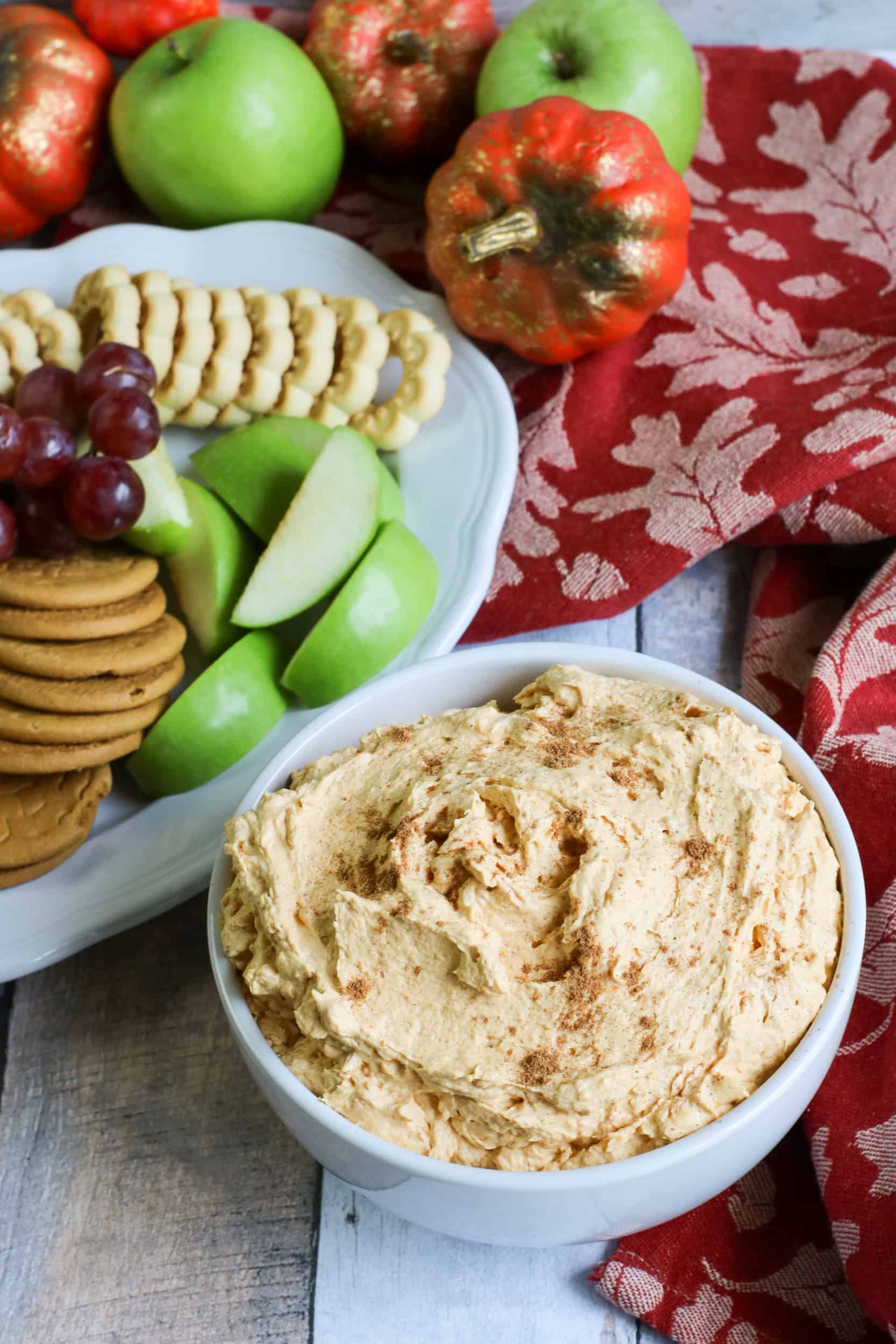 Bowl of pumpkin fluff with fruit & cookie platter behind it.