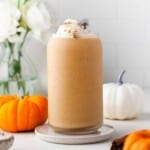 Smoothie with pumpkin spice and whipped cream on a white counter with mini pumpkins behind it.