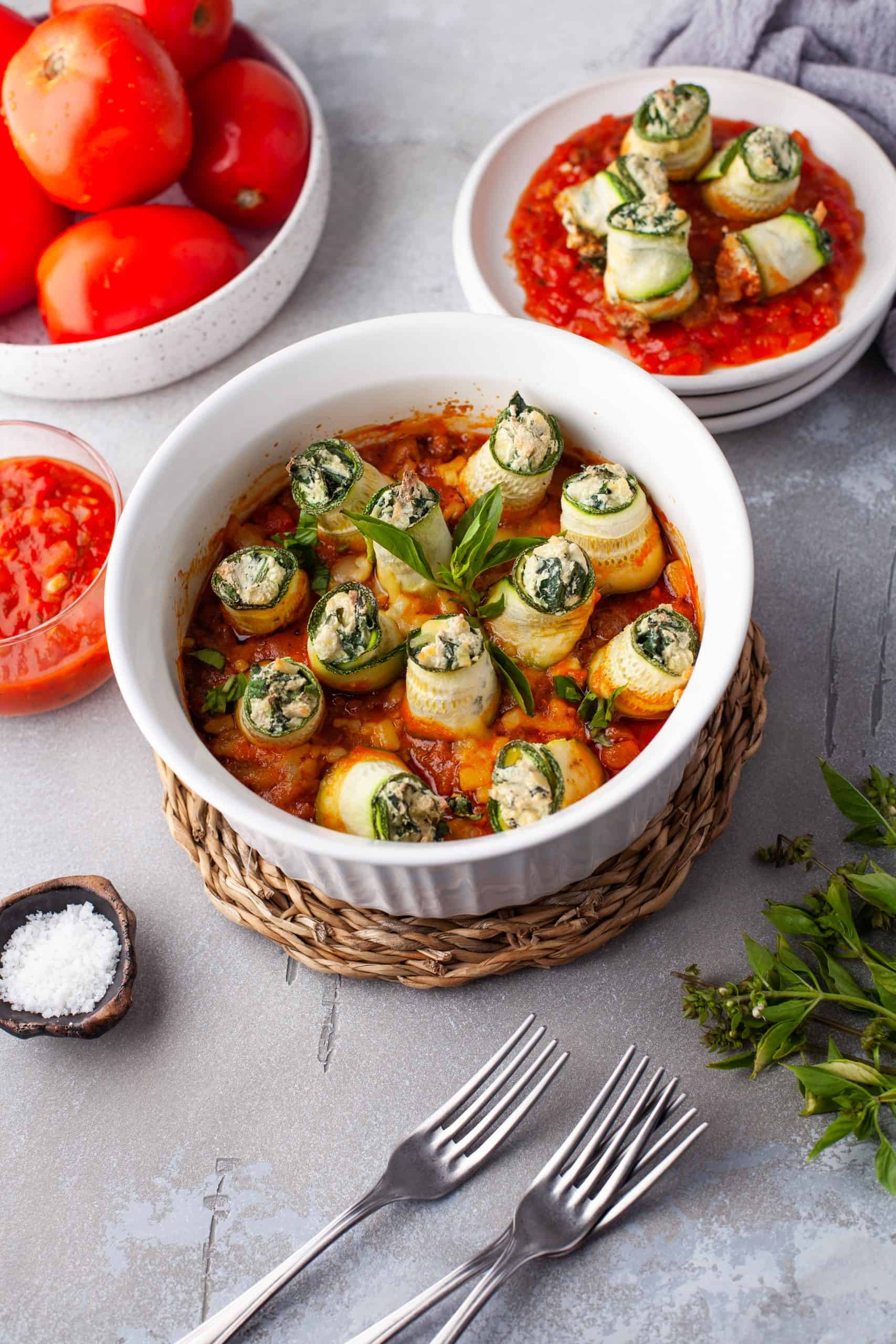 Zucchini Lasagna Rolls in a white bowl with an individual serving of them on the side.