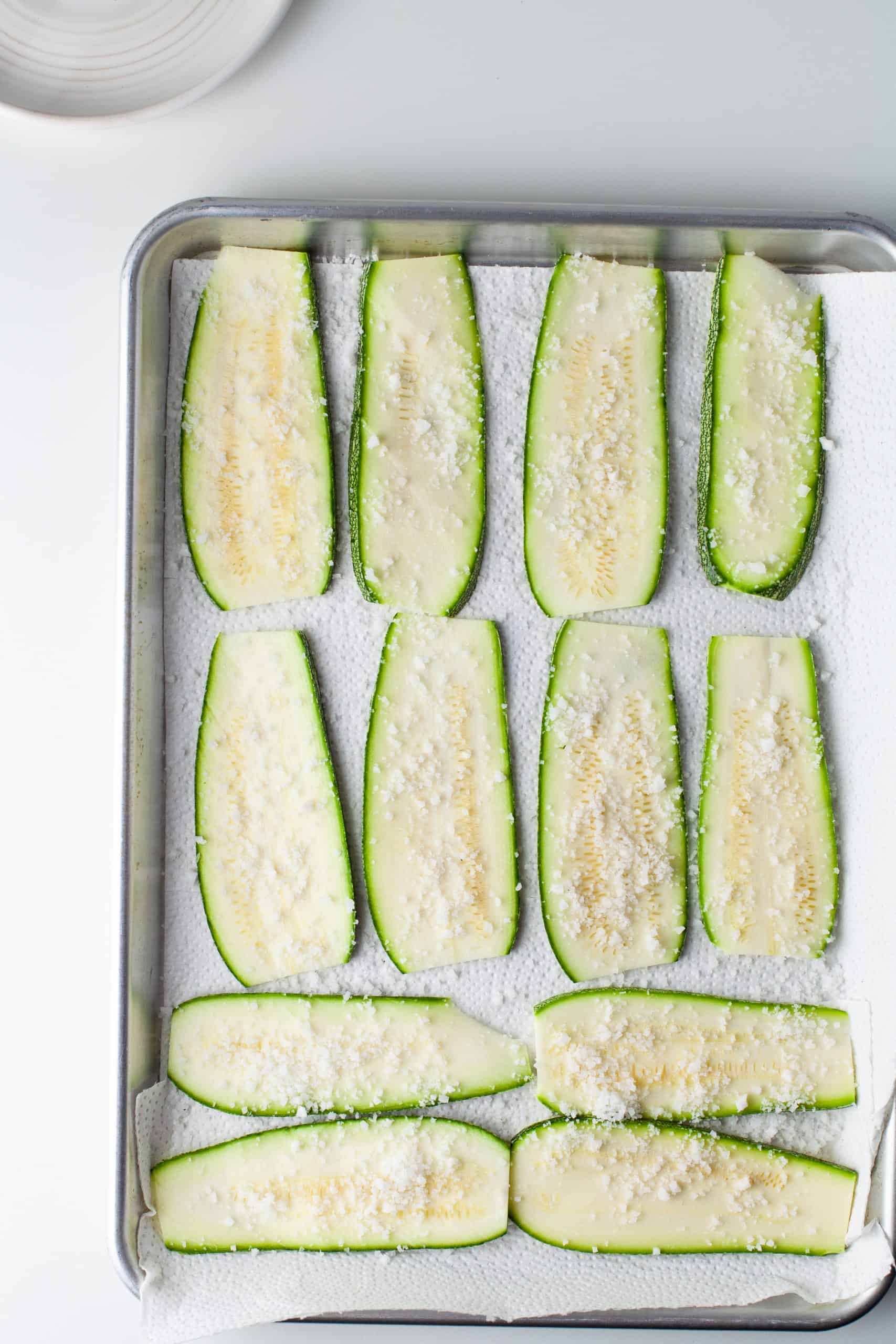 Salted zucchini slices on a sheet pan.