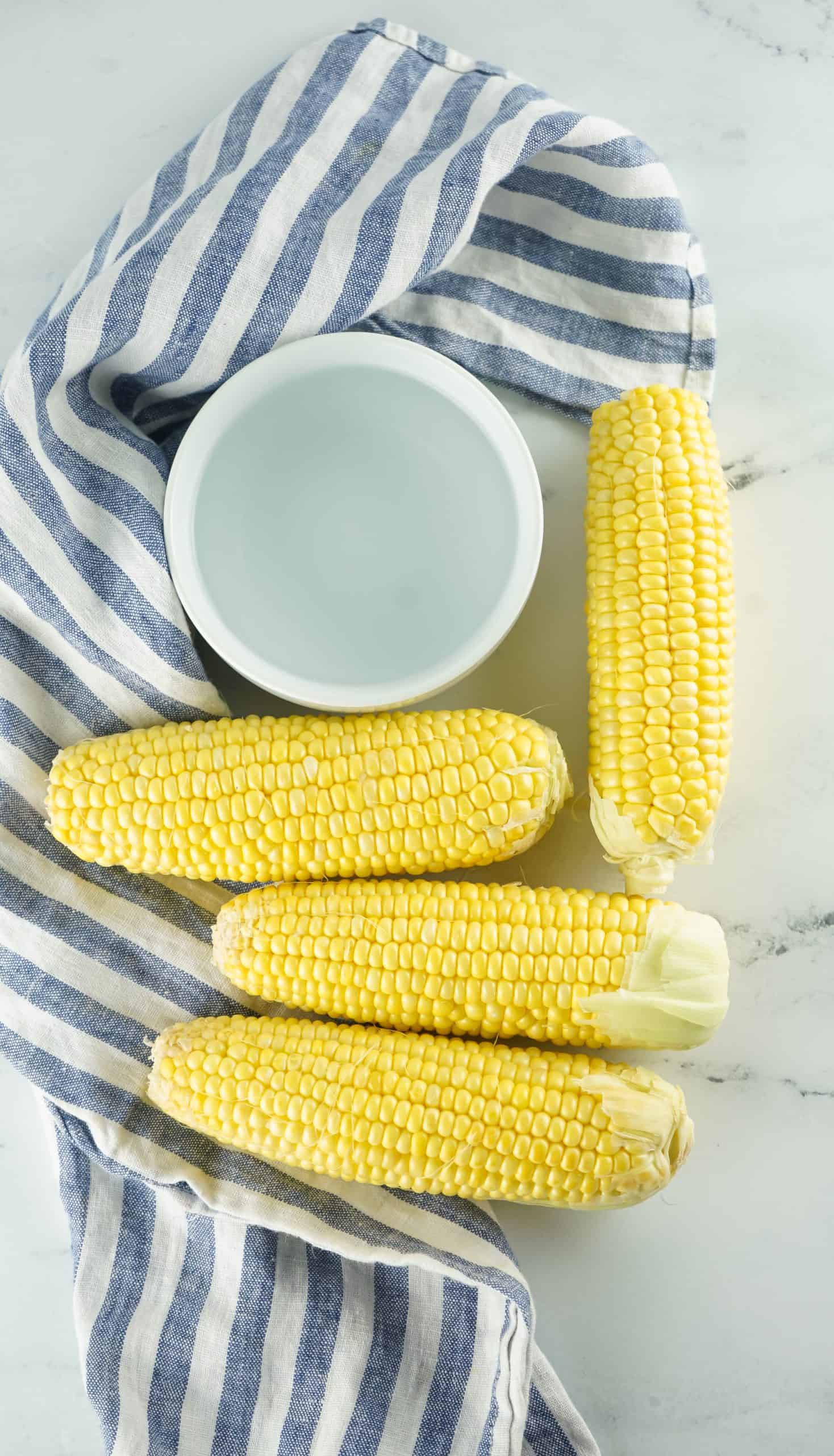 Overhead view of shucked corn and a bowl of water.
