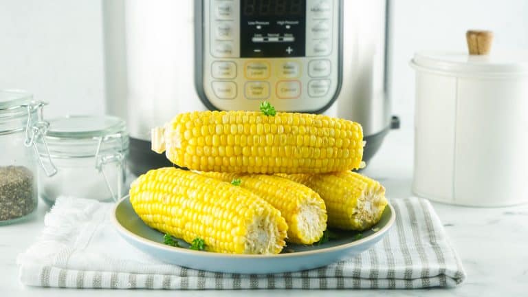 Cooked corn on a plate with parsley sprinkled on top in front of the Instant Pot.
