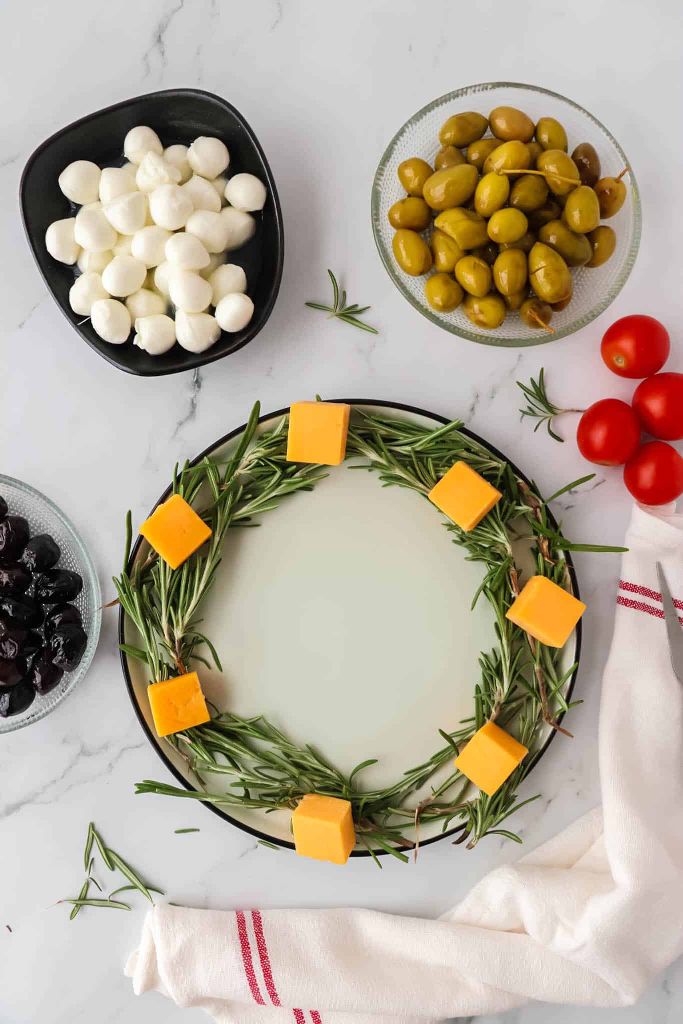 Cheese cubes in a circle on top of fresh rosemary sprigs in a circle on a plate.