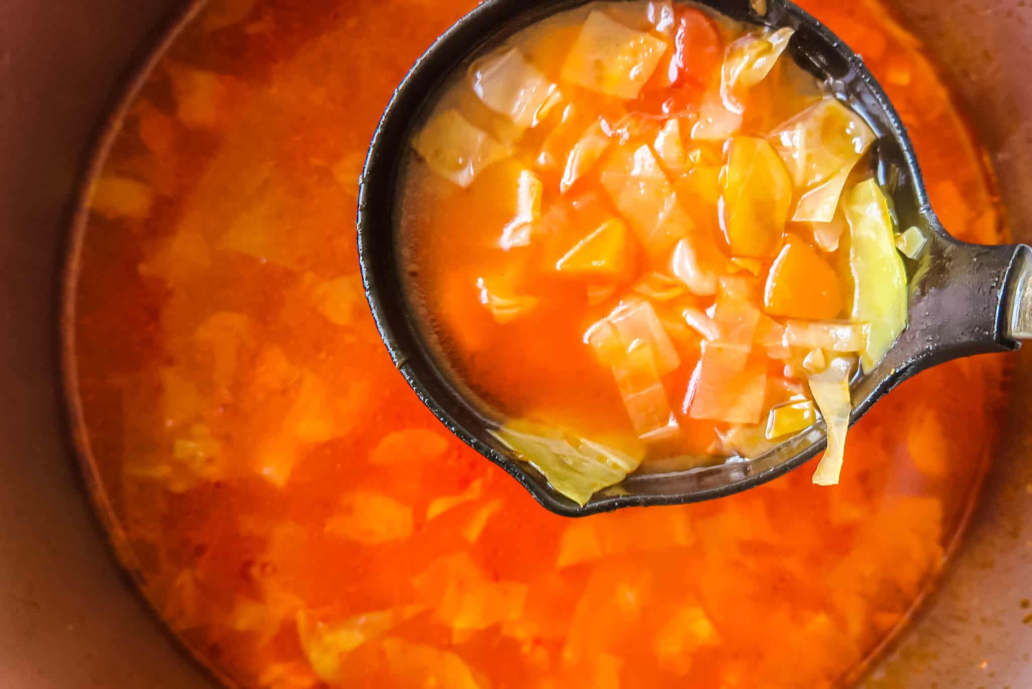 Low carb cabbage soup ladled out of pot.