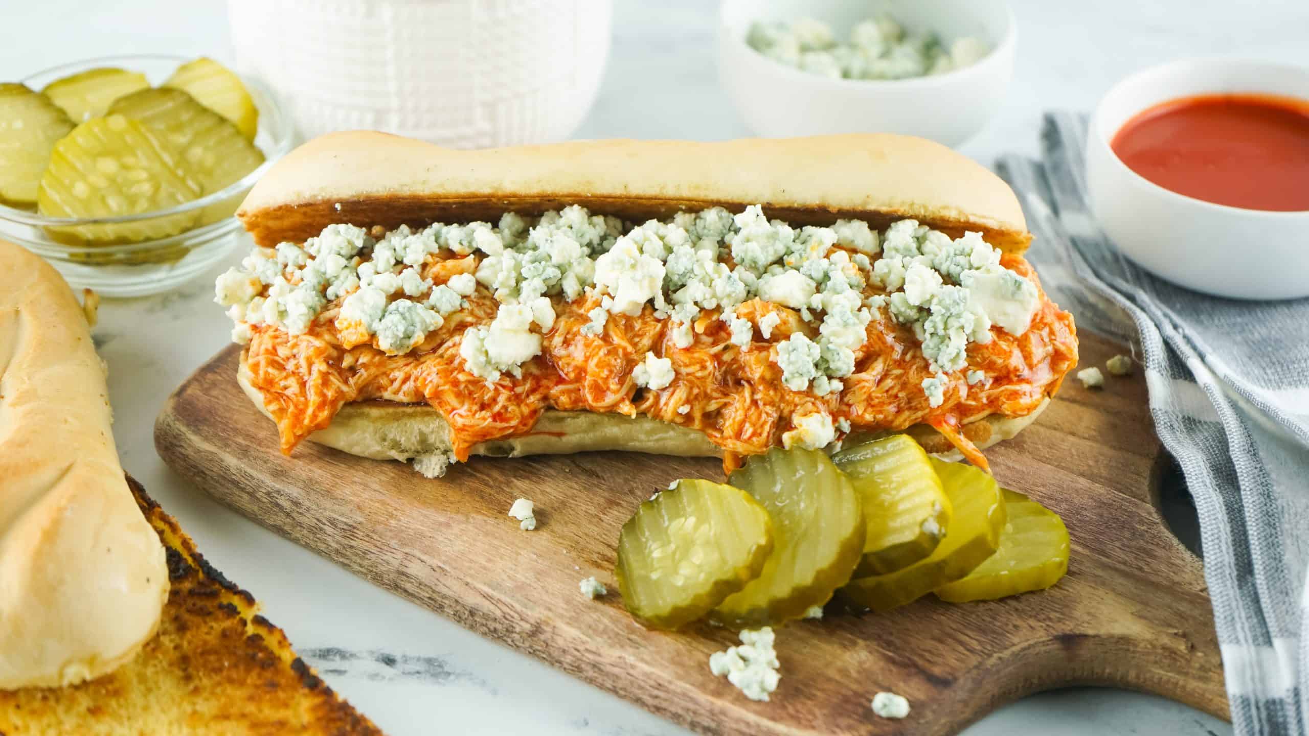 Buffalo Cheesesteak Sandwich on a cutting board with pickles on the side.