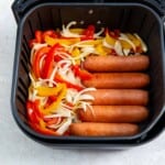 Overhead view of sausages, peppers and onions in an air fryer basket.