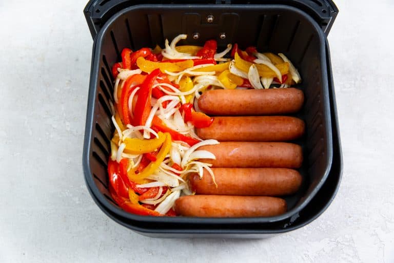 Overhead view of sausages, peppers and onions in an air fryer basket.