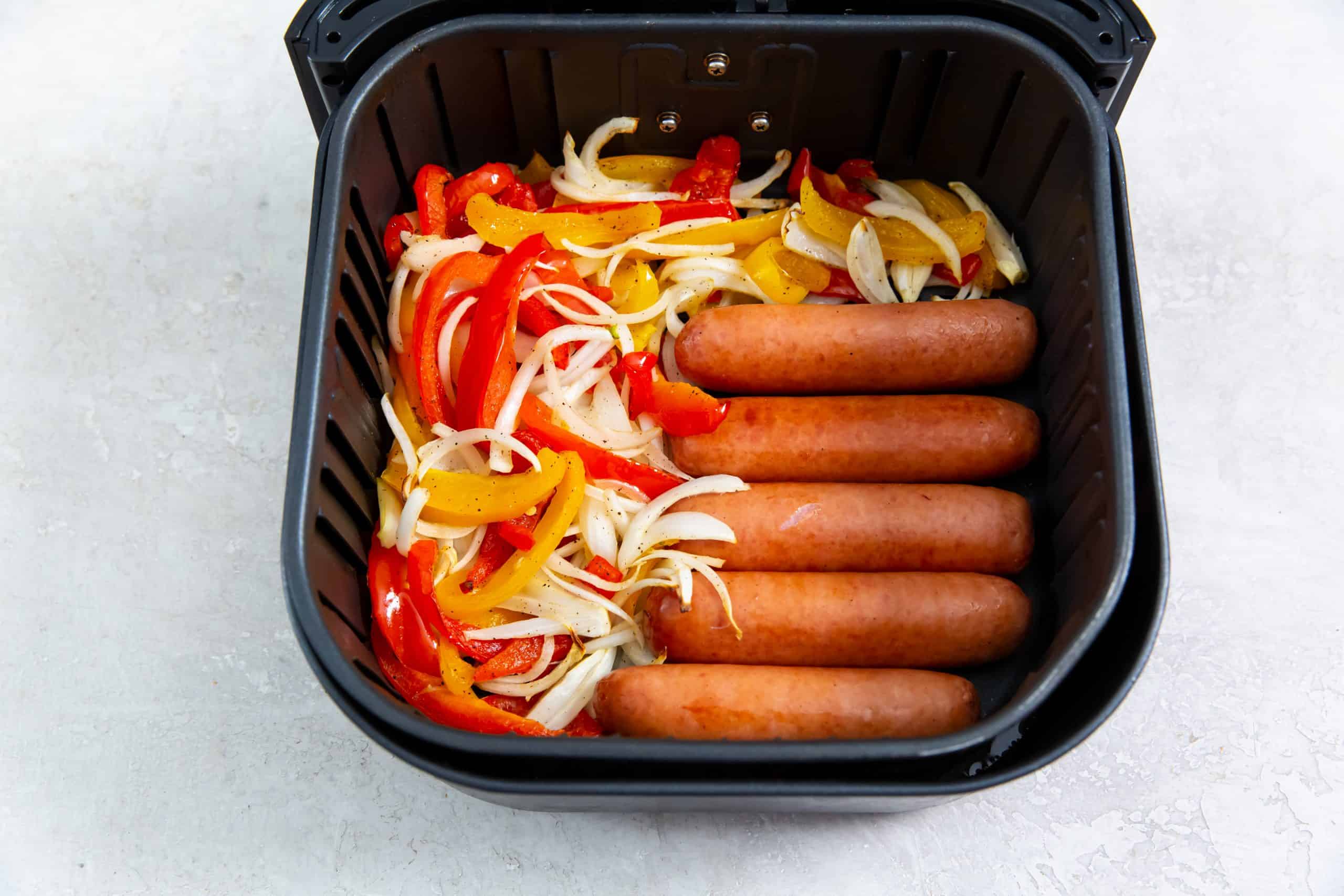 Overhead view of sausages, peppers and onions in an air fryer basket.